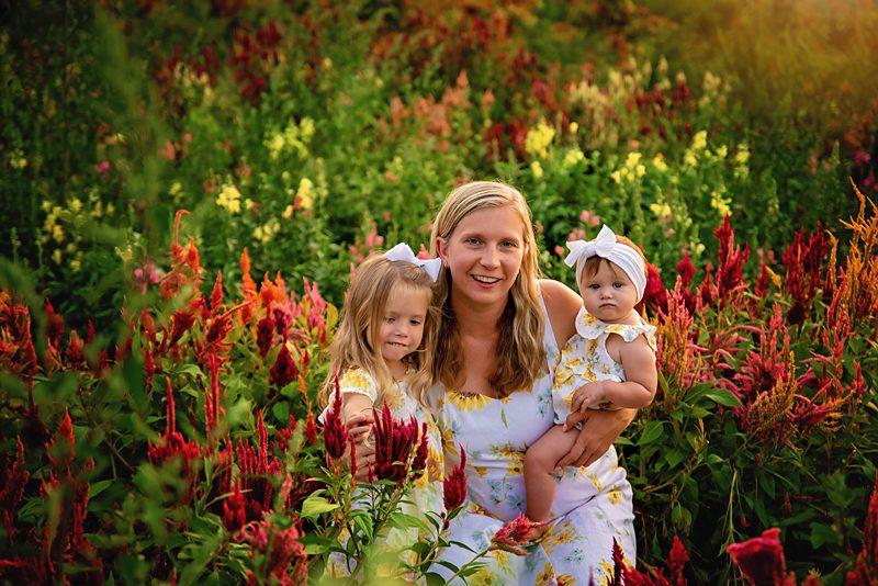 Mom with her two little girls their outfits are white dresses with yellow flowers and bows in their hair. Picture was taken at Tranquility farms in Northern New Jersey 