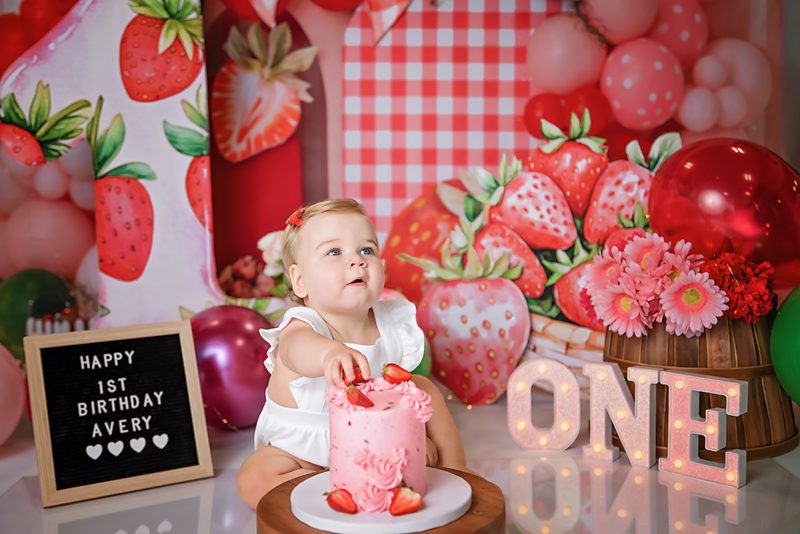 Blond baby picking up the strawberry off the cake during her photo shoot in Jefferson NJ