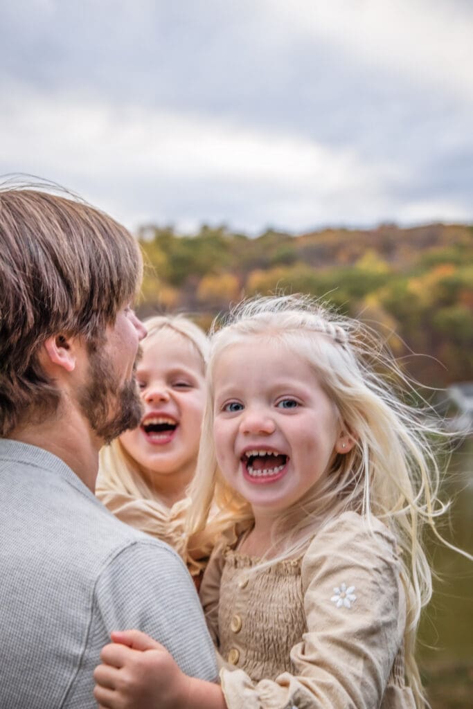 Little girls being twirled around in dads arms and laughing during their sun set photo shoot. In Jefferson NJ 